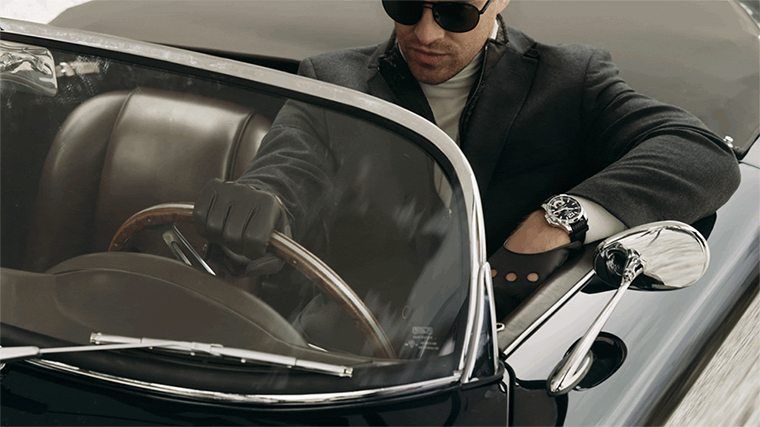 Egy férfi egy szép autót vezet a kezét kiteszi, amin egy drága óra van